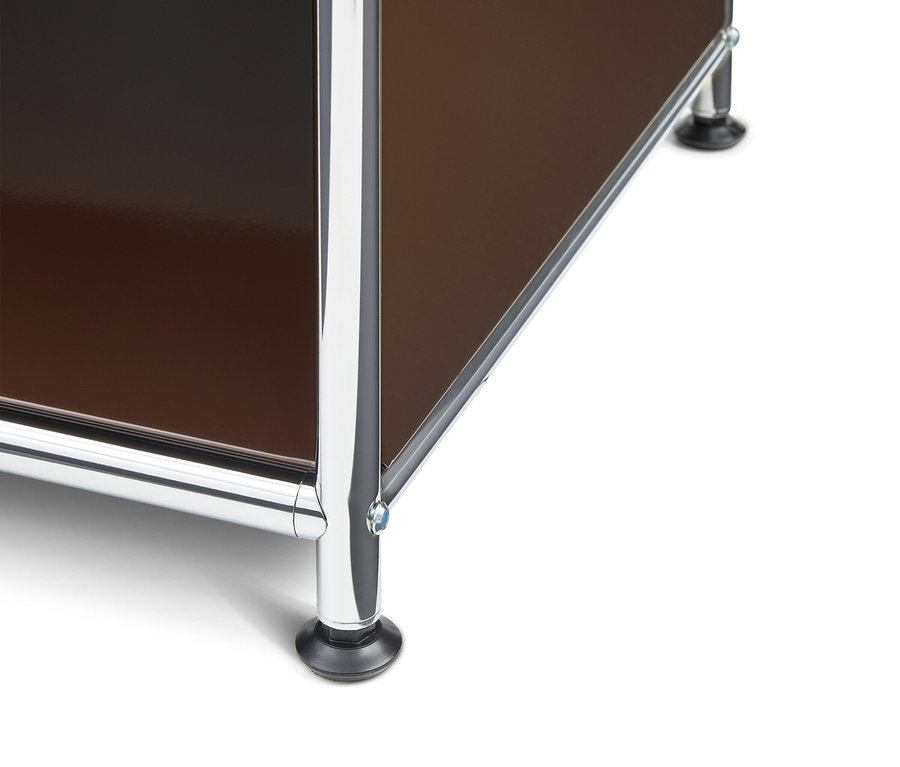 Nahaufnahme der unteren Ecke eines modularen Möbelstücks mit glänzenden braunen Platten und verchromten Metallrahmen, das auf schwarzen Füßen steht.