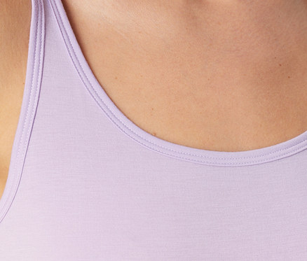 Nahaufnahme des oberen Brustbereichs und der Schulter einer Person, die ein hellviolettes Tanktop mit Rundhalsausschnitt trägt.