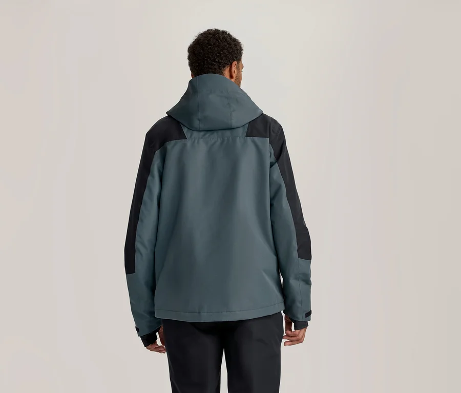 Eine Person von hinten, die eine dunkelgrau-türkise und schwarze Kapuzenjacke sowie eine schwarze Hose trägt.
