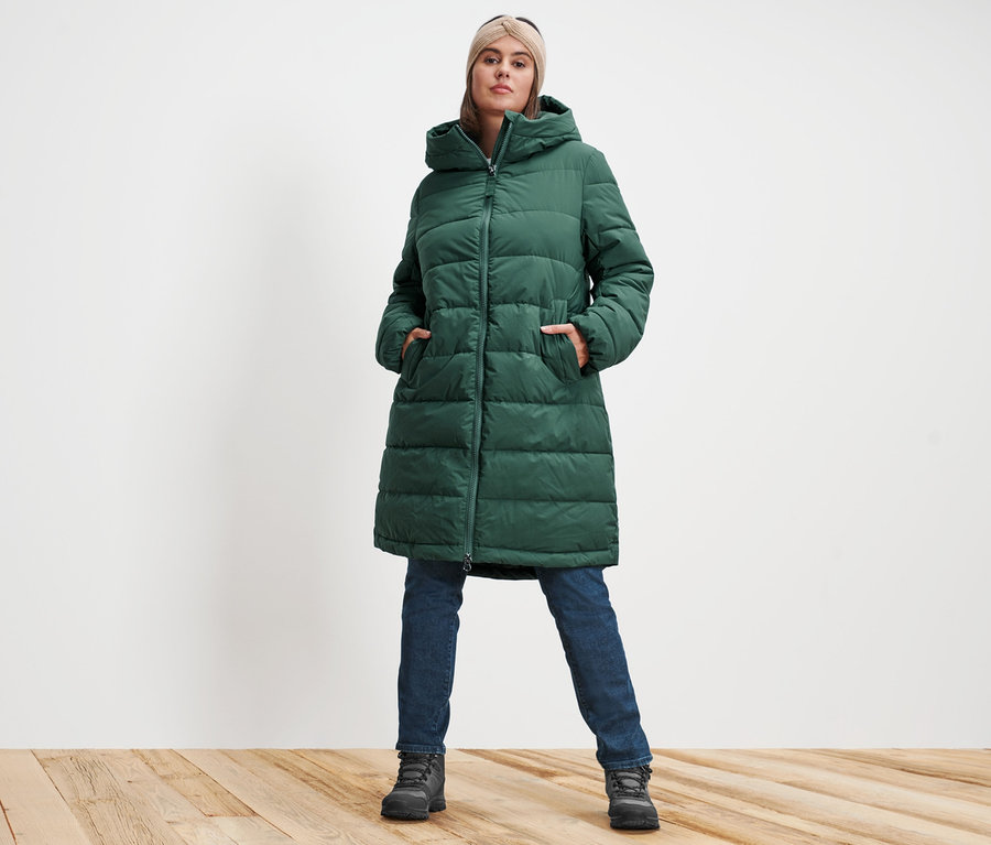 Frau posiert in grünem Steppmantel, sandfarbenem Strick-Stirnband und darkblue Denim Slim-Denim »Fit Emma«.