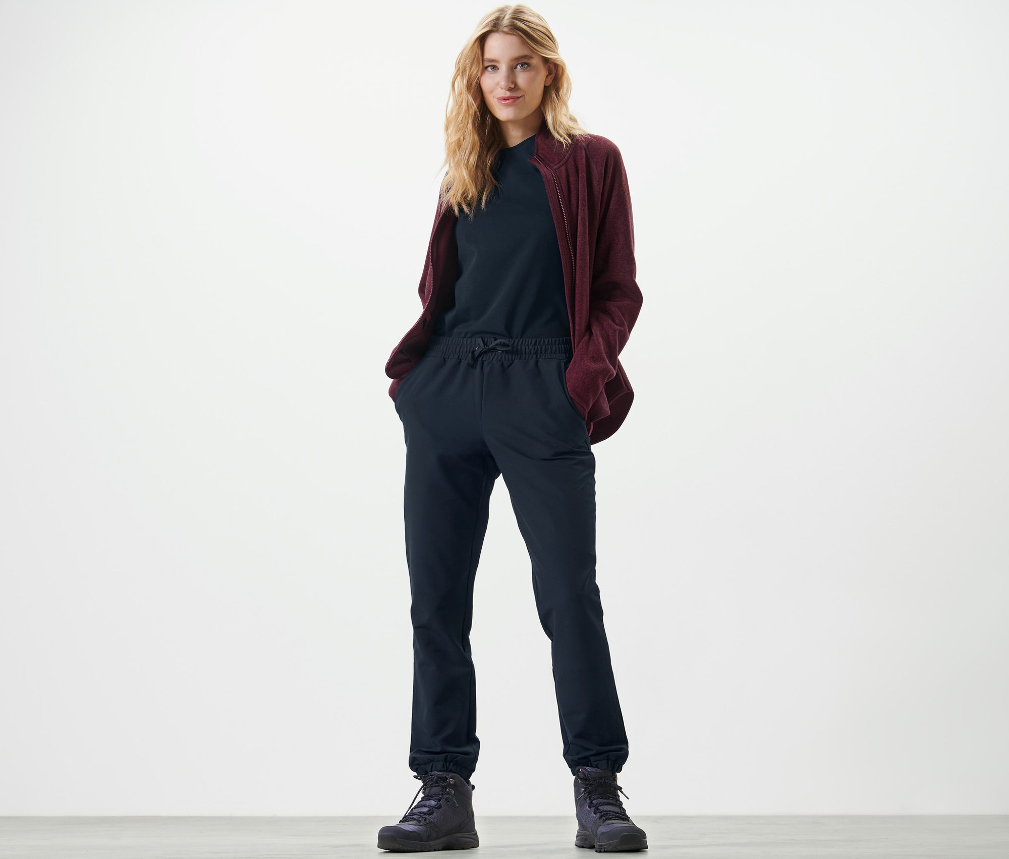 Blonde Frau steht mit Händen in den Taschen der Softshell-Joggpants.