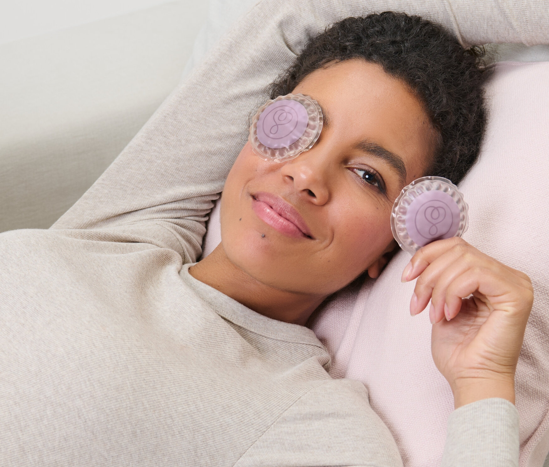 Frau liegt auf Couch mit 2 Augen-Kühlpads, eines auf dem Auge und eines in der Hand.
