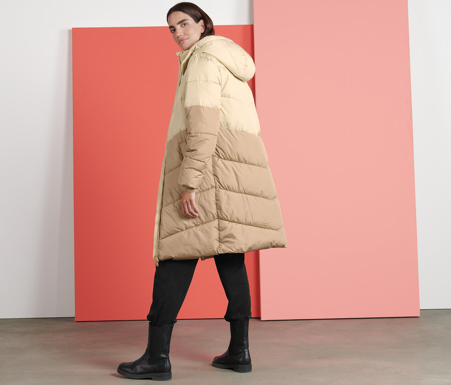 Frau trägt einen beige Steppmantel mit Kapuze.