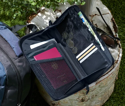 Geöffnete schwarze Dokumentenmappe liegt auf einem Baumstumpf neben einem blau-schwarzen Rucksack.