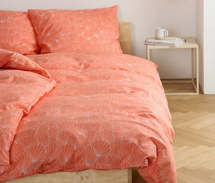 Auf einem Bett liegt Renforcé-Bettwäsche mit Blumenmuster.
