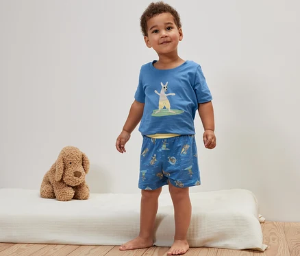 Ein Junge steht auf einer Matratze und trägt einen blauen Kinder-Shorty-Pyjama mit Känguru.