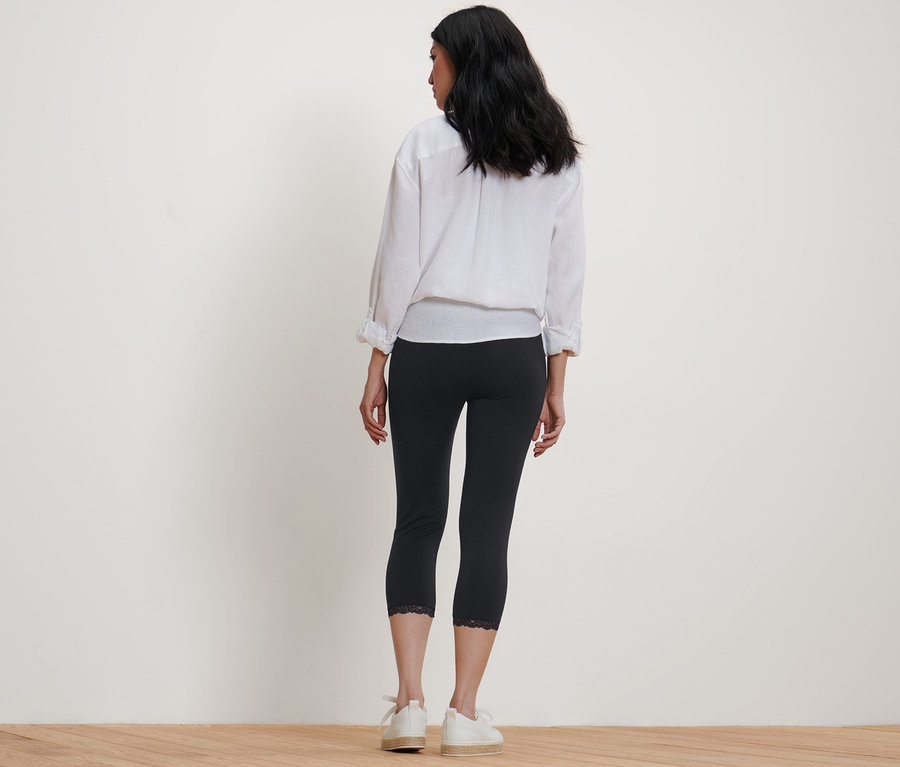 Frau steht mit dem Rücken zur Kamera und trägt eine schwarze 3/4-Leggings mit Spitzenborte.