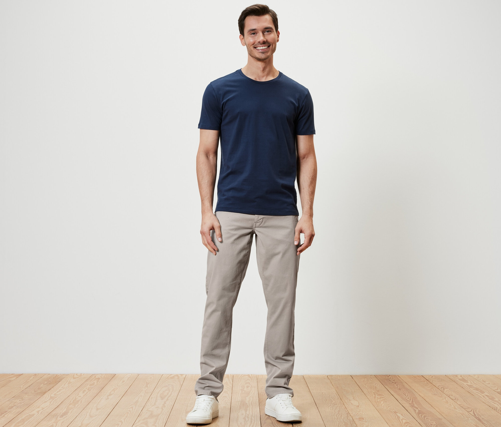 Mann steht und trägt eine 5-Pocket-Hose, ein T-Shirt und Turnschuhe.