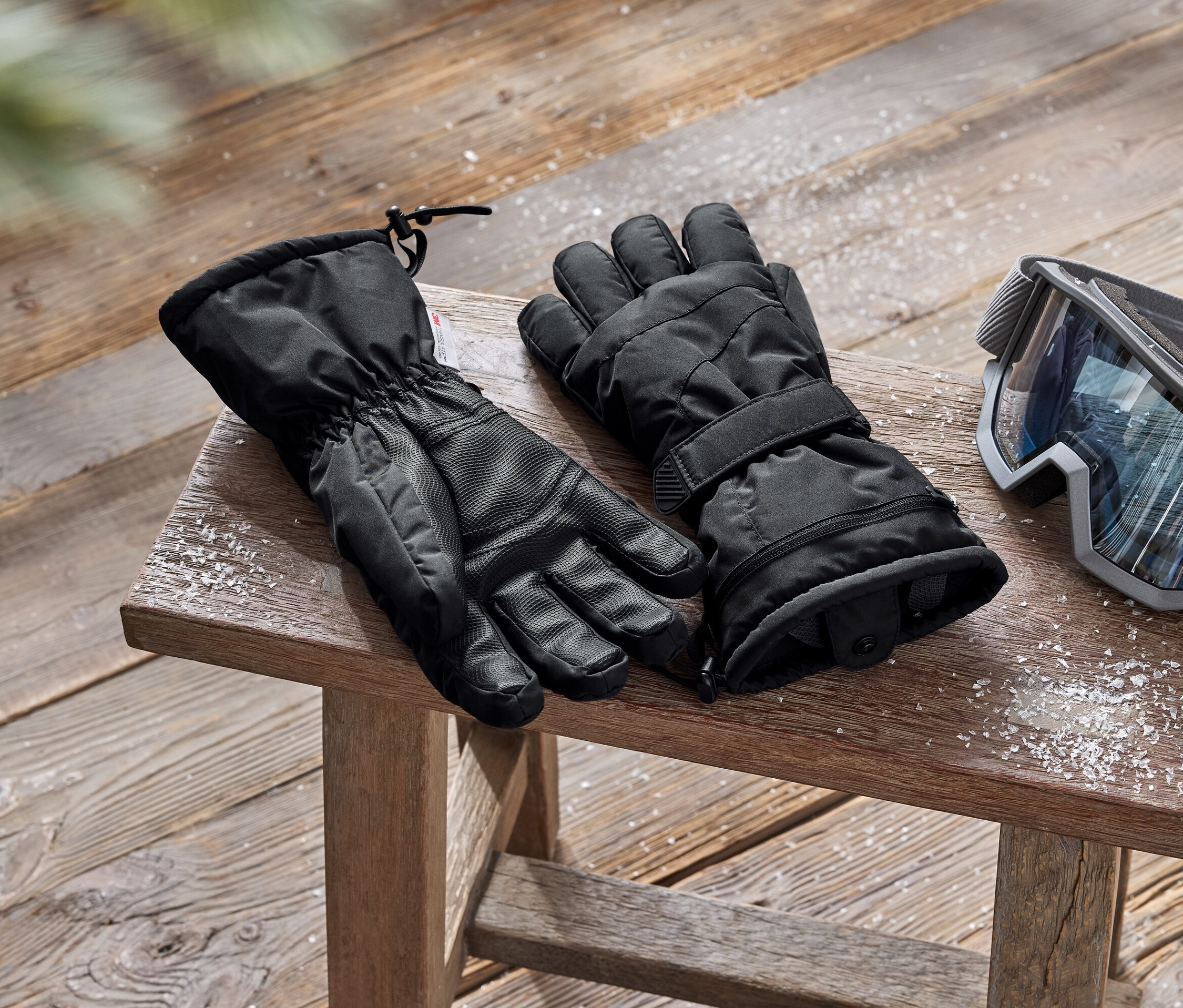 Schwarze Skihandschuhe und eine Skibrille liegen auf einem Holzhocker.