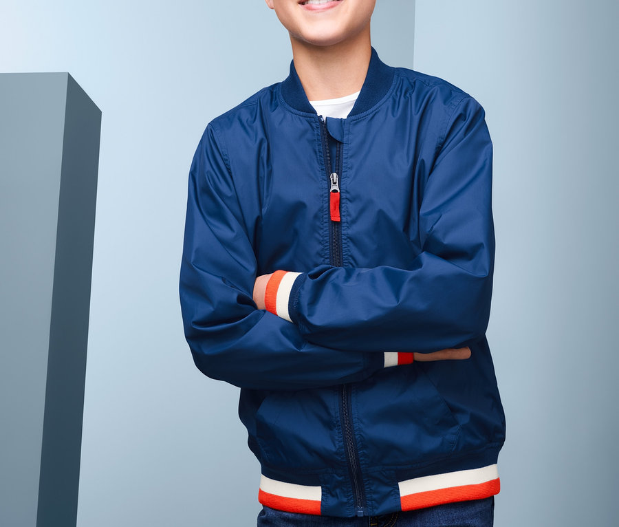 Ein lächelnder Junge posiert mit verschränkten Armen und trägt eine blaue Bomberjacke mit recyceltem Material.