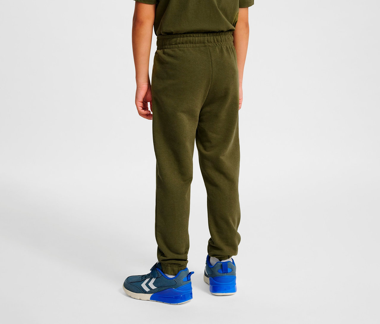 Junge von hinten trägt eine grüne HUMMEL HMLJR Base Regular Pants und blaue Schuhe.