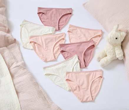 Auf einem weißen Hintergrund liegen sieben Damenslips in verschiedenen Rosa- und Weißtönen. Daneben liegen ein Plüschhase und ein rosa Kissen.