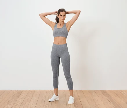 Frau posiert in grauem Sport-BH und Leggings.