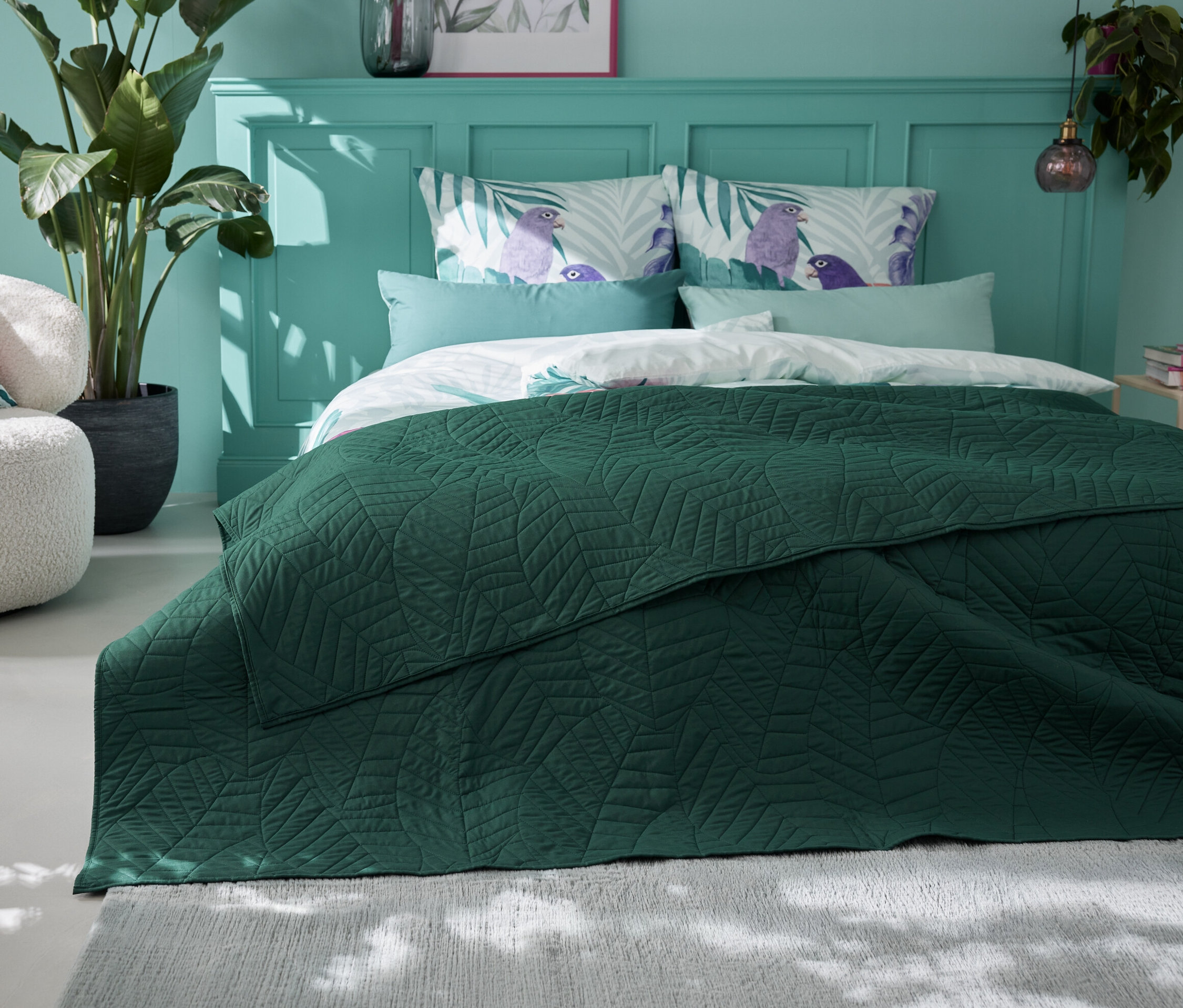 Ein grüner, gesteppter Bettüberwurf (230 x 250 cm) liegt auf einem Bett in einem Schlafzimmer.
