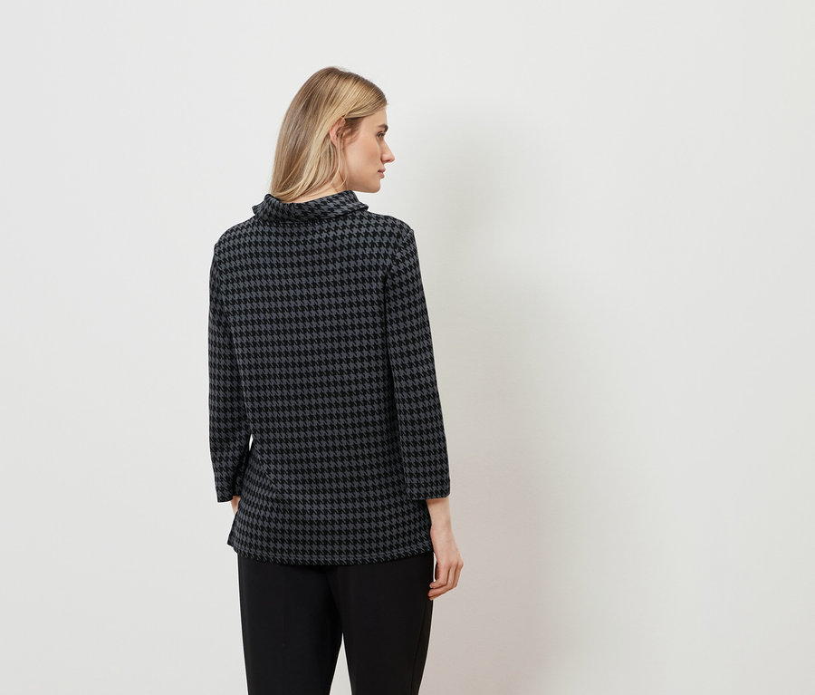 Eine Frau von hinten trägt eine Hahnentrittbluse und eine schwarze Hose.