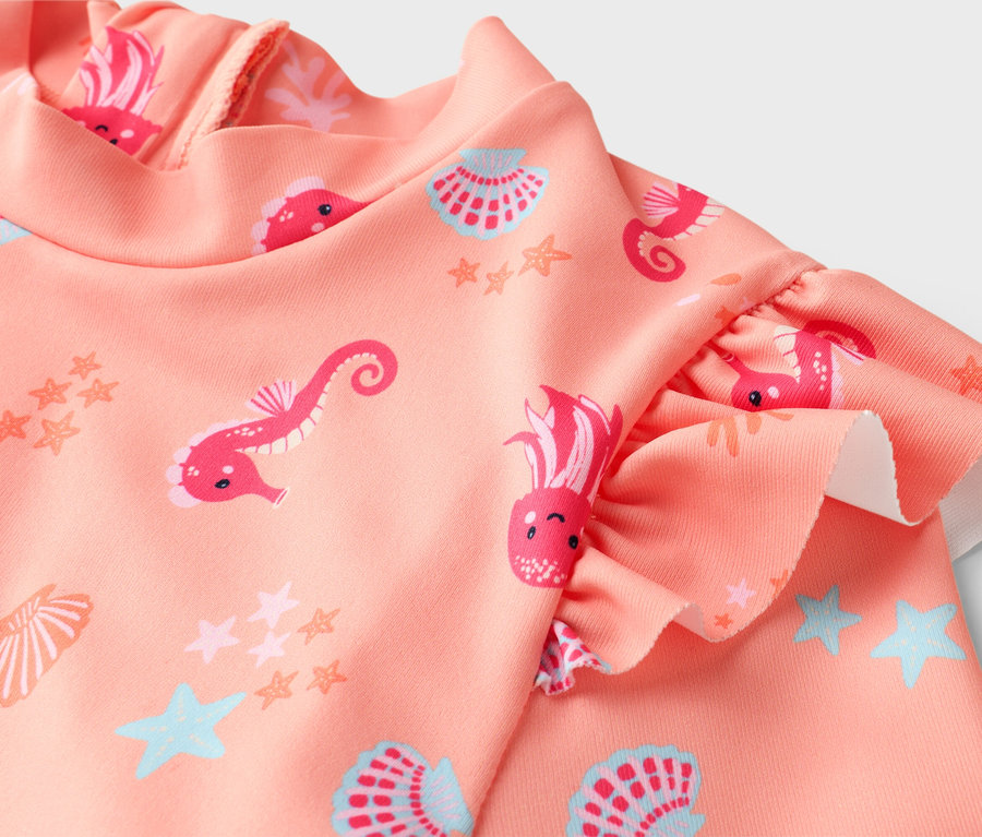 Nahaufnahme eines rosafarbenen Kinderbadeanzugs mit Rüschenärmeln und einem Allover-Muster aus Seepferdchen, Quallen, Sternen und Muscheln.