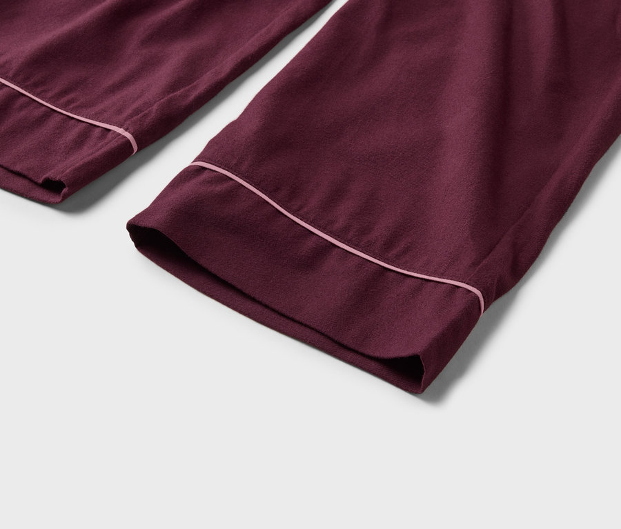 Nahaufnahme von zwei burgunderroten Pyjamahosen mit rosa Paspelierung an den Beinabschlüssen.