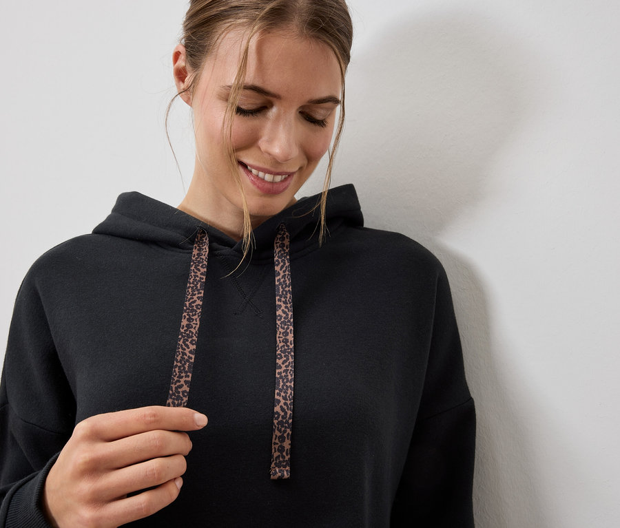 Frau trägt einen schwarzen Hoodie mit Leopardenmuster-Kordeln.