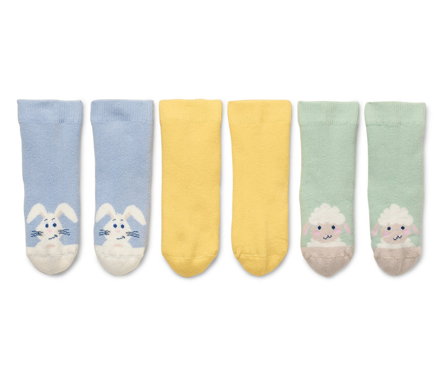 Zwei blaue Socken mit Hasen, zwei gelbe Socken und zwei grüne Socken mit Schafen liegen auf einem weißen Hintergrund.