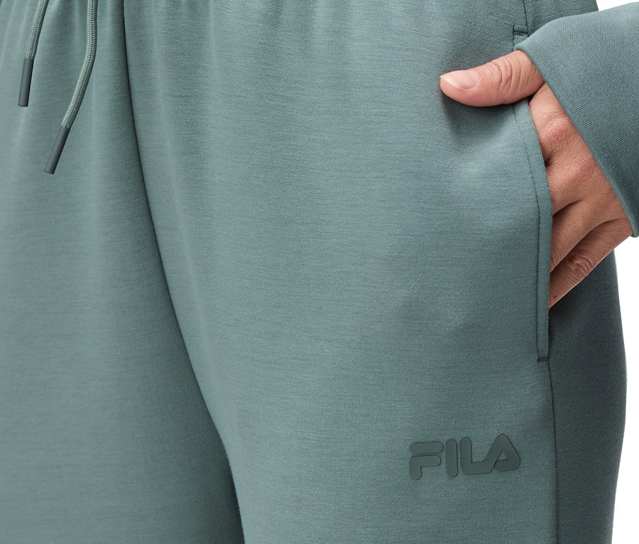 Nahaufnahme einer Person, die eine grüne Fila-Jogginghose mit elastischem Bund und Kordelzug sowie einer Hand in der Hosentasche trägt.