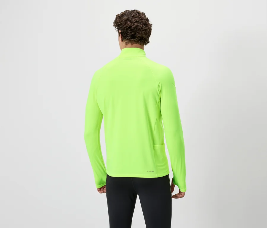 Rückansicht einer Person mit lockigem Haar, die ein neongrünes Langarmshirt und eine schwarze Hose vor einem weißen Hintergrund trägt.
