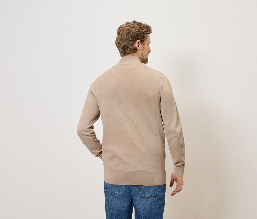Mann mit beigem Strickpullover und Jeans, von hinten gesehen.