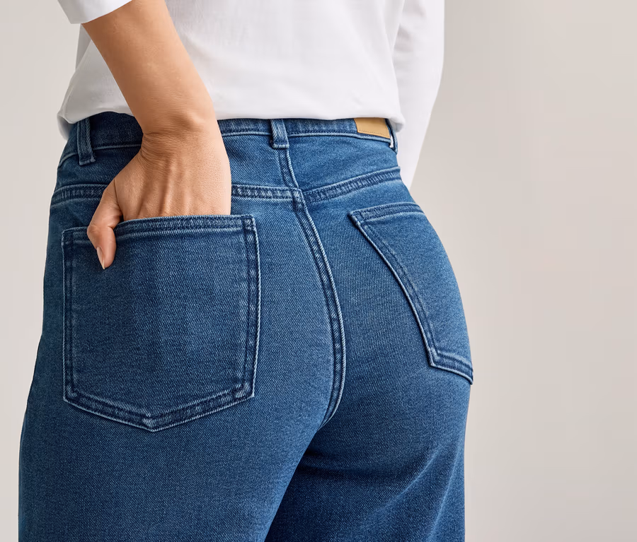 Frau mit Hand in der Gesäßtasche einer blauen Jeans, dazu ein weißes Oberteil.