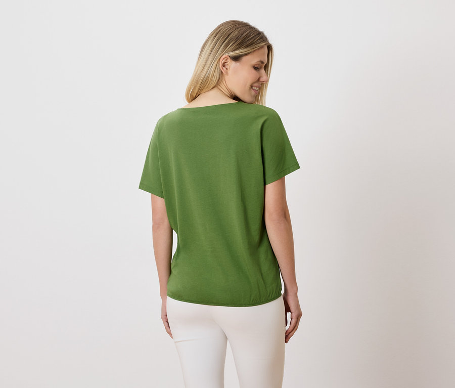 Eine Frau mit blonden Haaren trägt ein grünes T-Shirt und weiße Hosen.