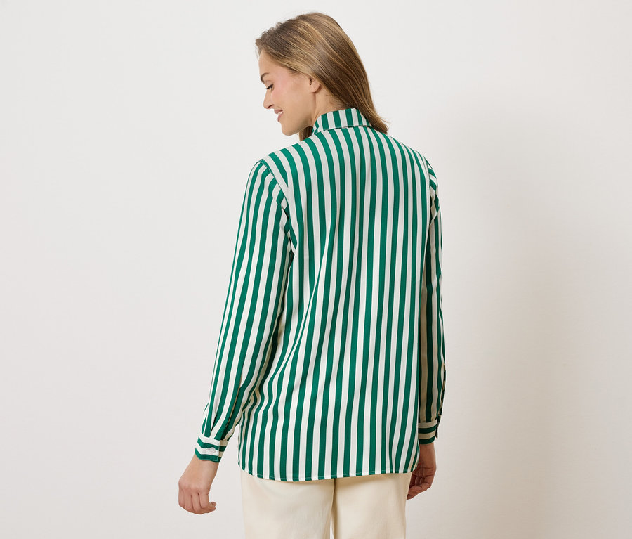 Eine Frau von hinten, die eine grün-weiß gestreifte Bluse und beigefarbene Hosen trägt.