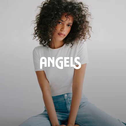 Frau mit lockigem Haar, weißem T-Shirt und hellblauer Jeans sitzt und blickt in die Kamera. Der Schriftzug ANGELS ist über dem Bild.