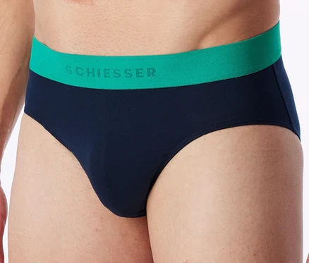 Nahaufnahme eines Mannes, der marineblaue Slips mit einem grünen Bund trägt, auf dem „SCHIESSER“ steht.