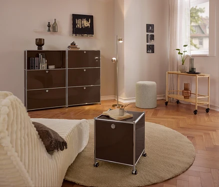 Modernes Wohnzimmer mit beigem Sofa, großer brauner Metall-Kommode »CN3« mit 3 Klappenfächern, kleinem braunen Metall-Rollcontainer »CN3« mit 2 Klappenfächern auf rundem Teppich, Bouclé-Sitzhocker und Servierwagen aus Holz.