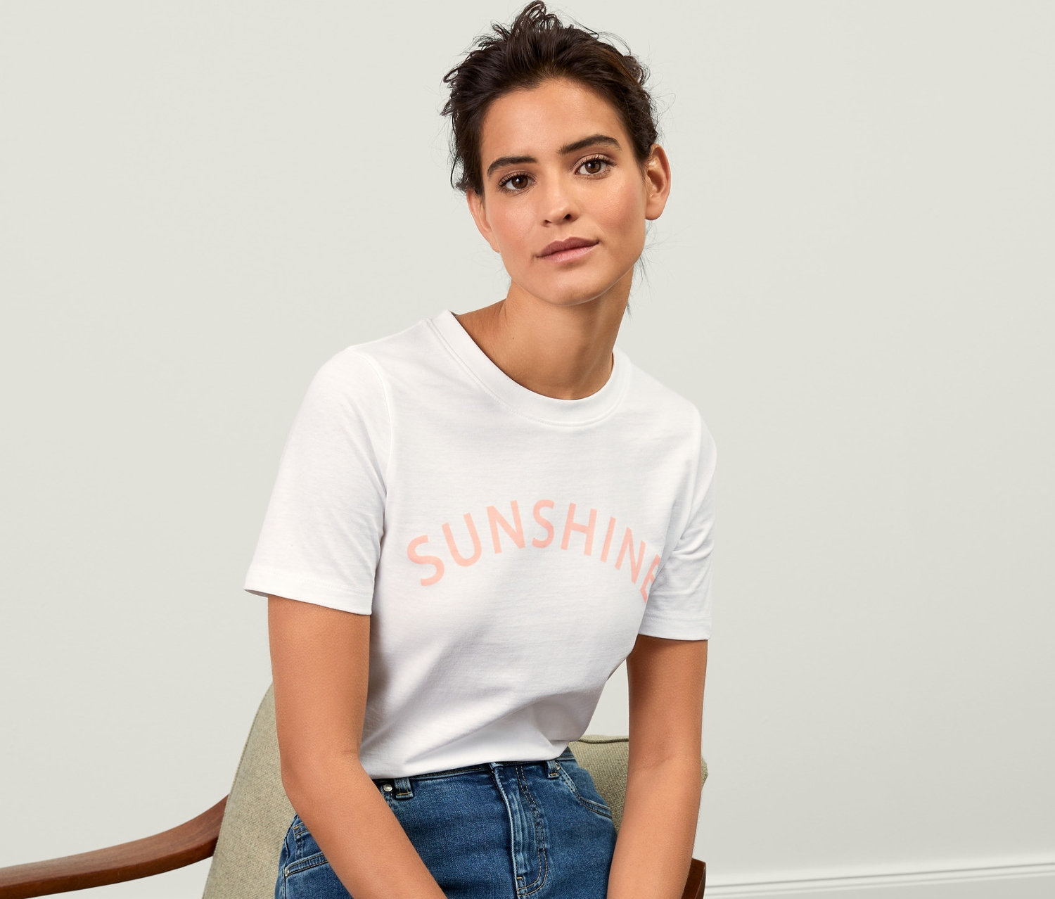 Frau sitzt auf einem Stuhl und trägt ein T-Shirt mit Print.