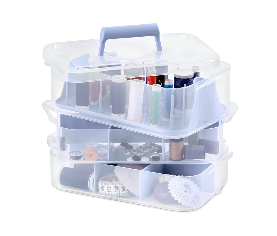 Ein dreistöckiger Organizerboxen aus durchsichtigem Kunststoff, gefüllt mit bunten Nähgarnen, Knöpfen und Nähzubehör.