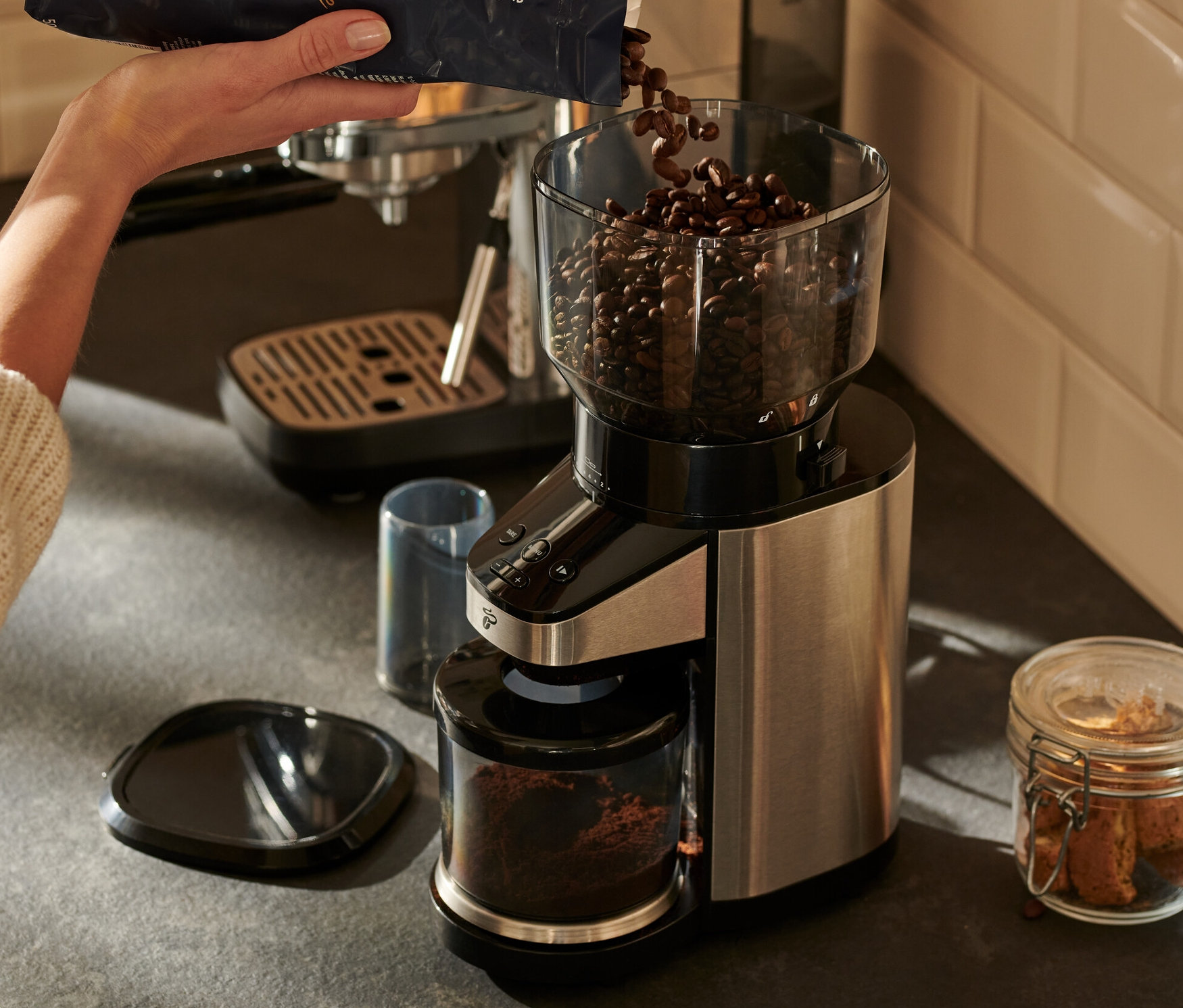 Frau schüttet Kaffeebohnen in eine elektrische Kaffeemühle mit Waage.