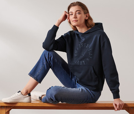 Frau sitzt auf einer Bank und trägt einen dunkelblauen Hoodie.