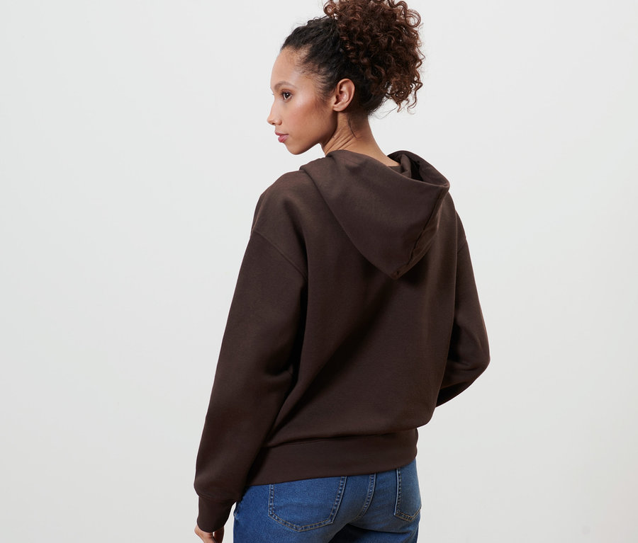 Frau posiert mit dem Rücken zur Kamera und trägt einen dunkelbraunen Hoodie.