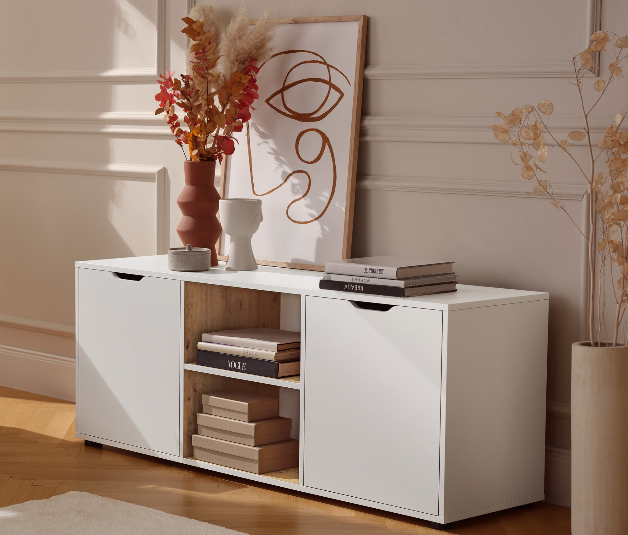 Ein Beistelltisch aus Metall steht neben einem Sideboard mit Schubladen. Im Hintergrund steht ein cremefarbenes Federkern Eck-Schlafsofa »Jenna«.