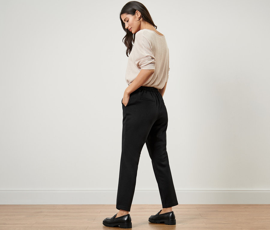 Frau trägt beigen Pullover und schwarze Joggpants.