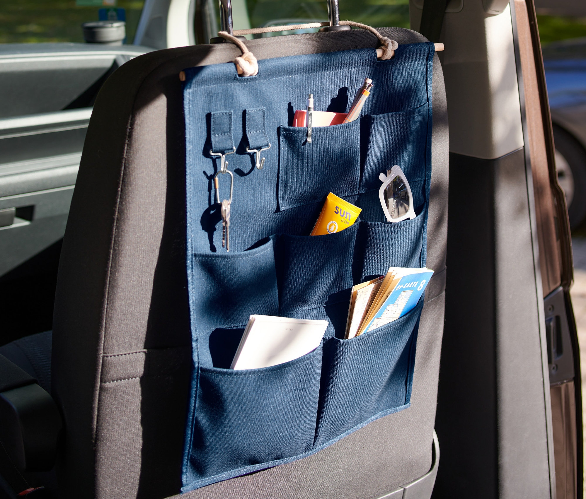 Ein blauer Hänge-Organizer mit Taschen hängt an der Rückseite eines Autositzes.