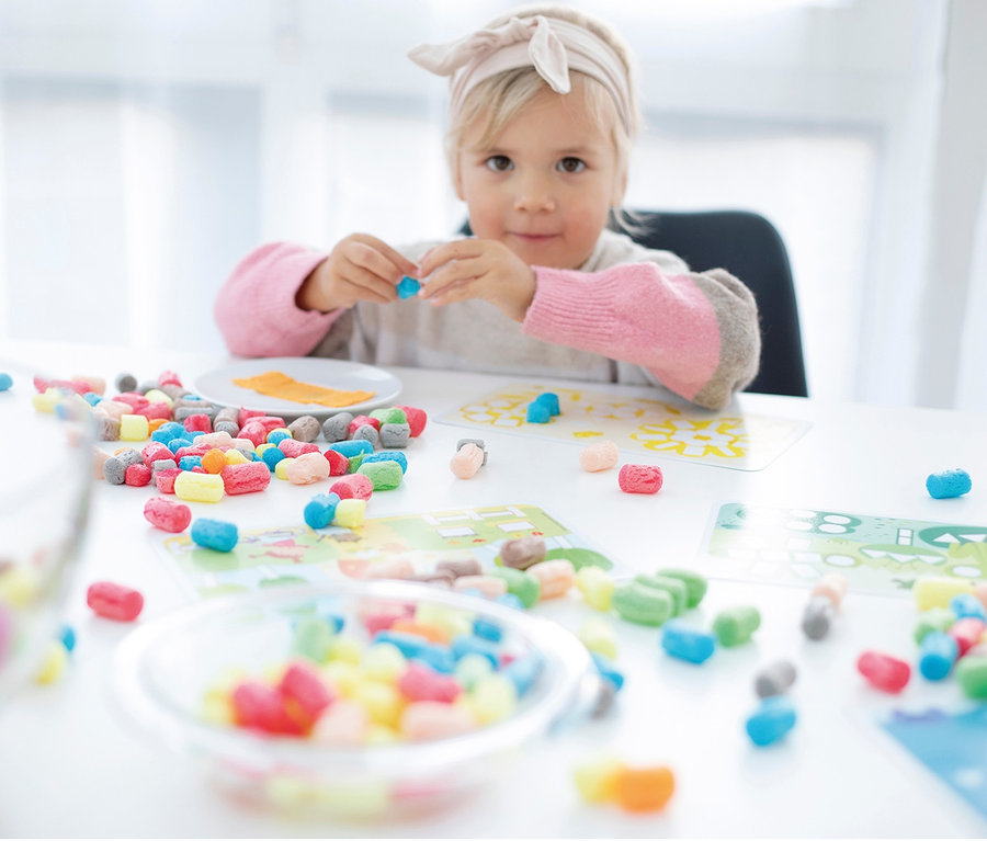 Mädchen spielt mit buntem PlayMais®-Set am Tisch.