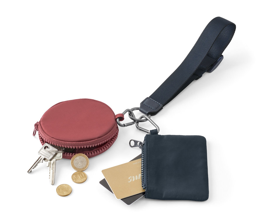 Weinrotes, rundes Portemonnaie mit Schlüsseln und Münzen neben einem blauen Reißverschluss-Portemonnaie mit Karten und Multifunktions-Schlüsselband.