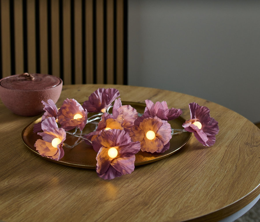 LED-Lichterkette mit Blumen liegt auf einem goldenen Teller auf einem Holztisch.