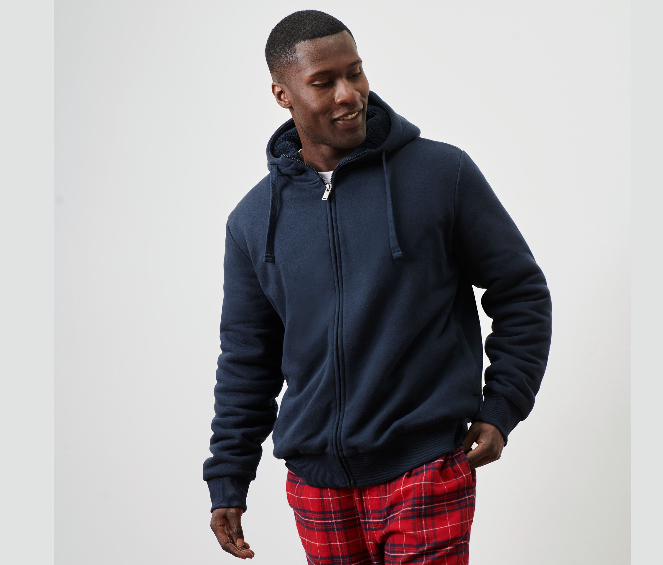 Mann trägt eine Kapuzen-Sweatjacke mit Teddyplüsch-Futter und karierte Hose.