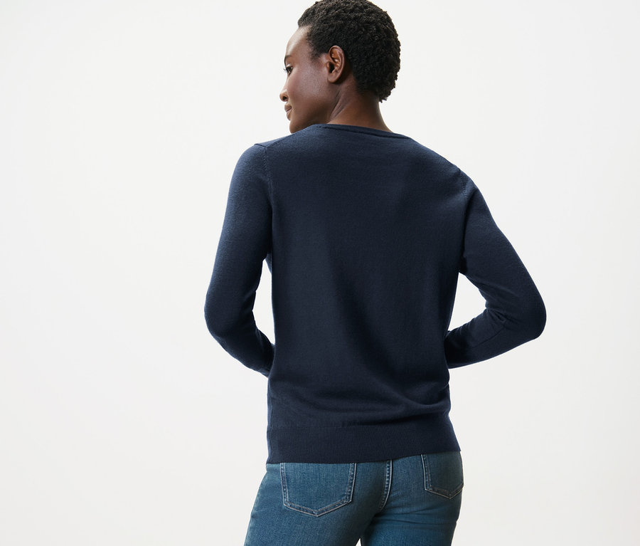 Rückansicht einer Frau, die einen dunkelblauen Merino-Feinstrickpullover und blaue Jeans trägt.