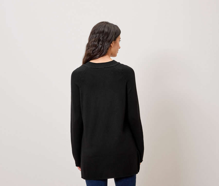 Rückansicht einer Frau mit dunklem, gewelltem Haar, die einen schwarzen Pullover und blaue Jeans trägt.