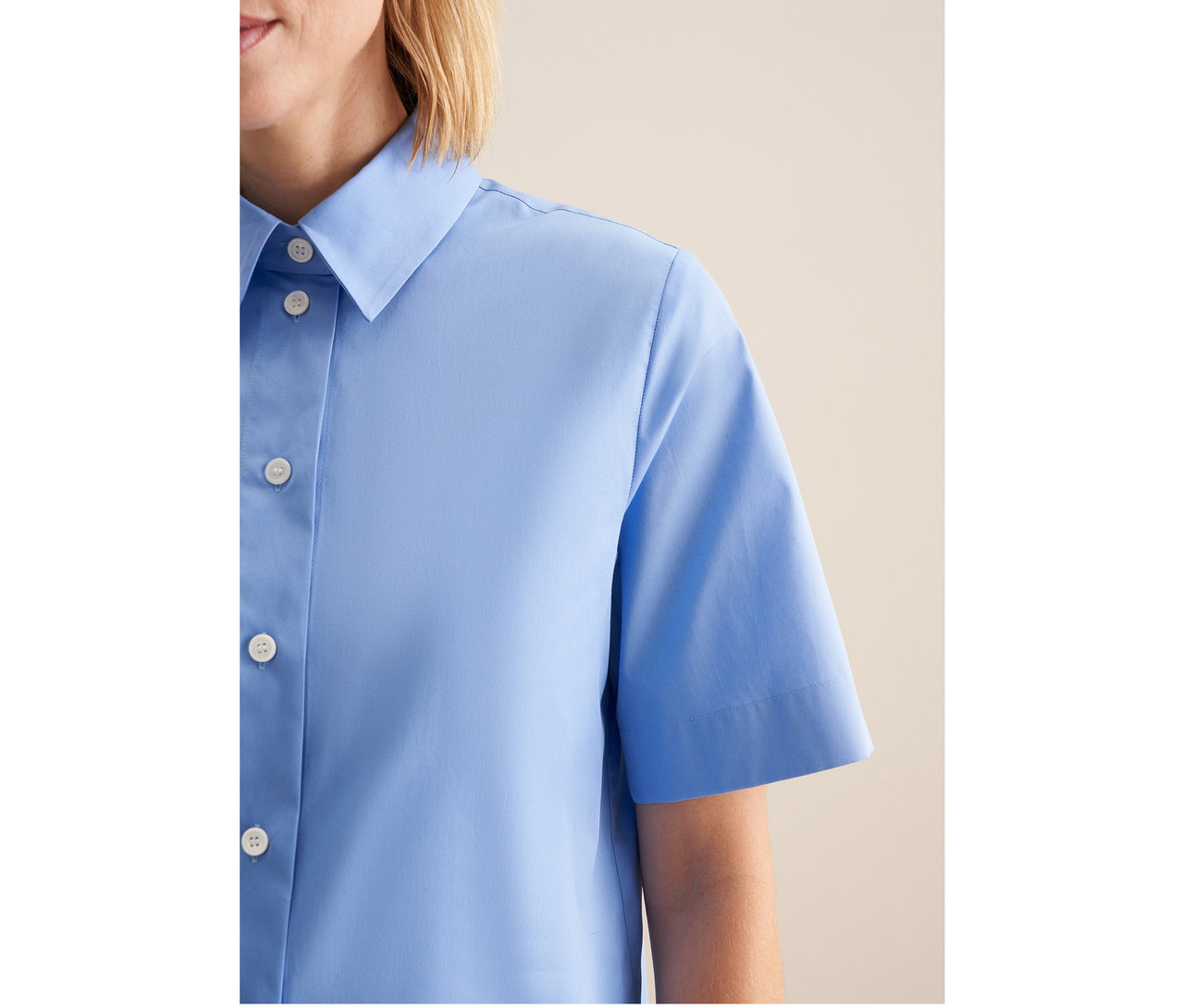 Nahaufnahme einer Frau in einer hellblauen Seidensticker Kurzarm-Bluse mit Kragen und weißen Knöpfen.