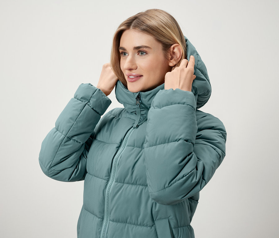 Frau richtet Kapuze an türkisfarbener Daunenjacke.