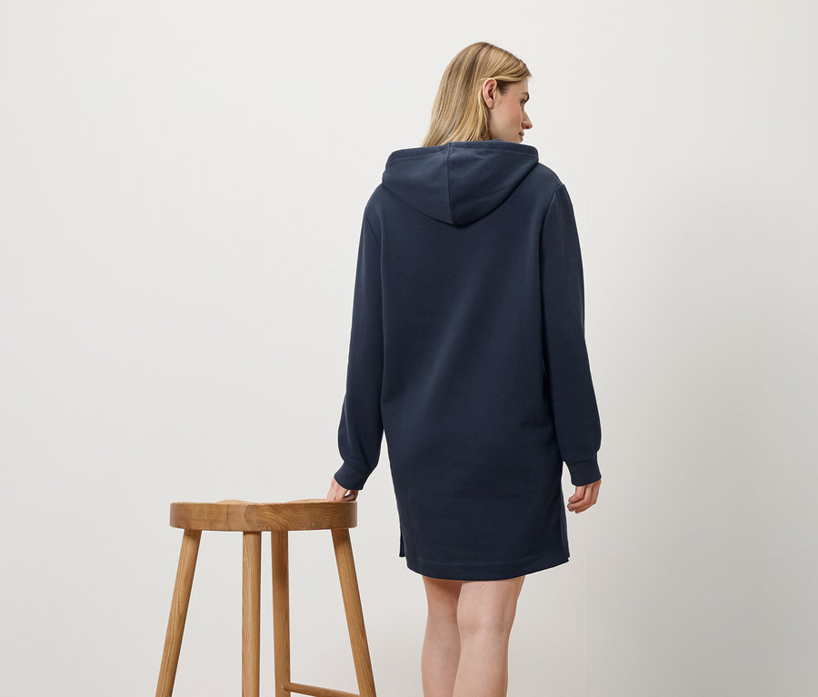 Eine Frau in einem marineblauen Kapuzenkleid steht neben einem Holzhocker.