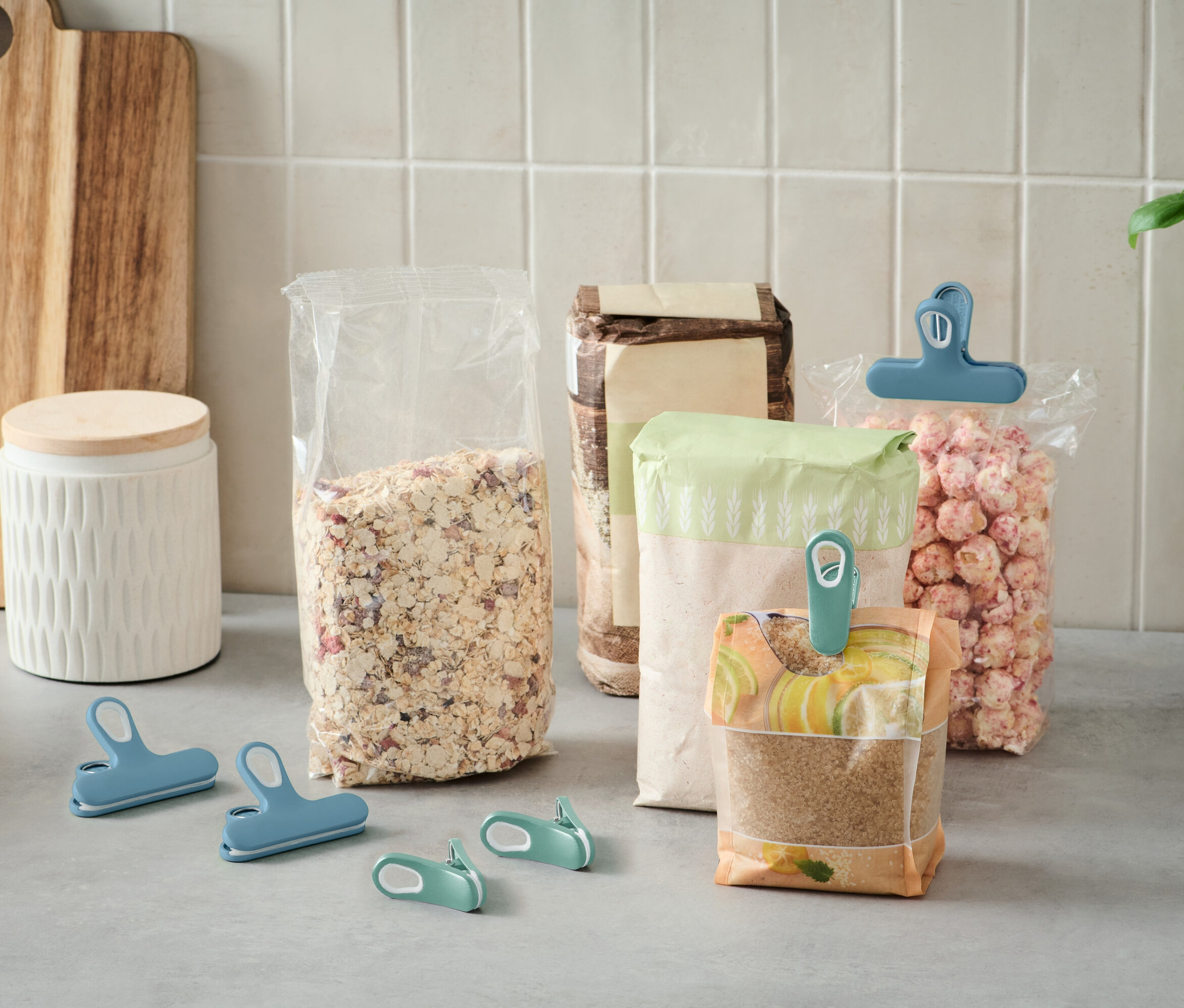 Mehrere offene Lebensmittelbeutel stehen auf einer Küchentheke und sind mit bunten Clips verschlossen.